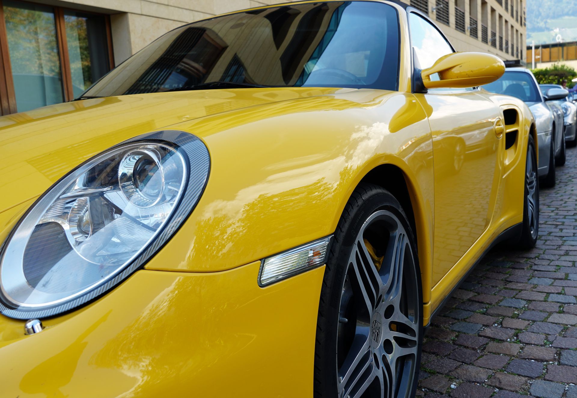A yellow sports car is parked on a cobblestone street