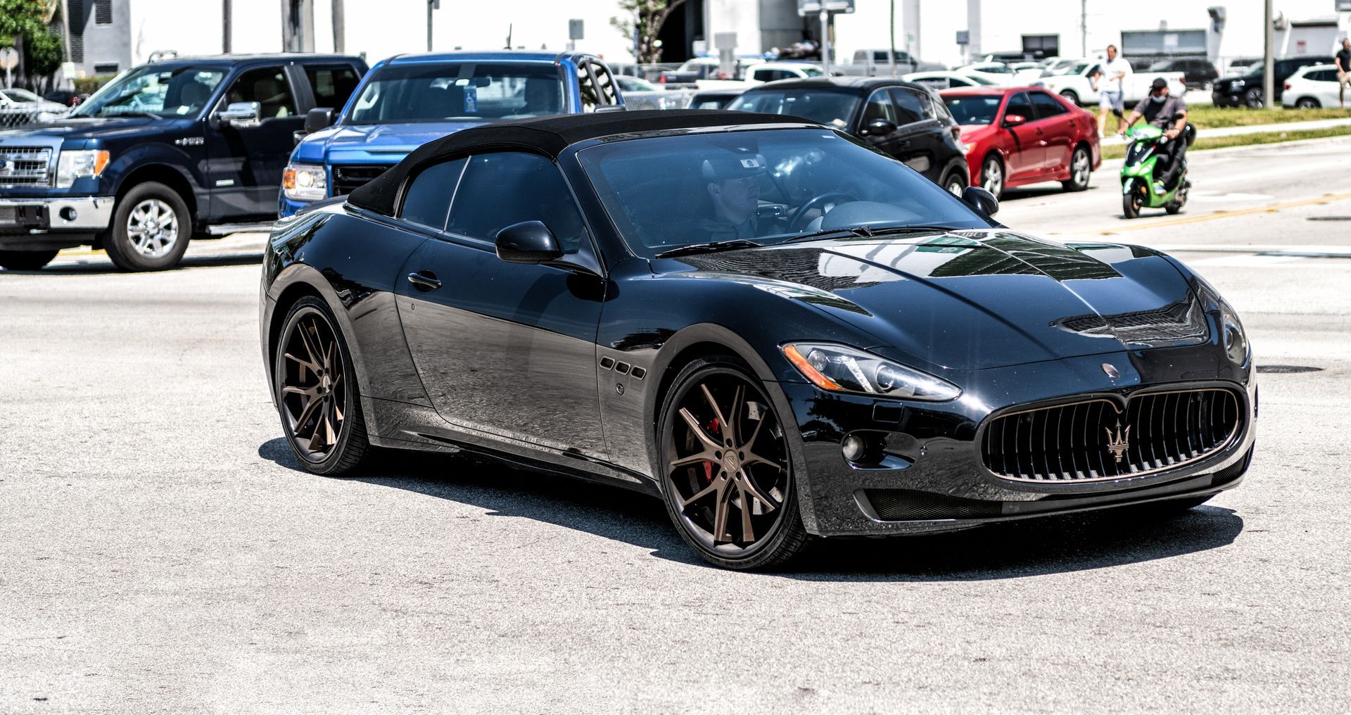 A black maserati convertible is parked in a parking lot.