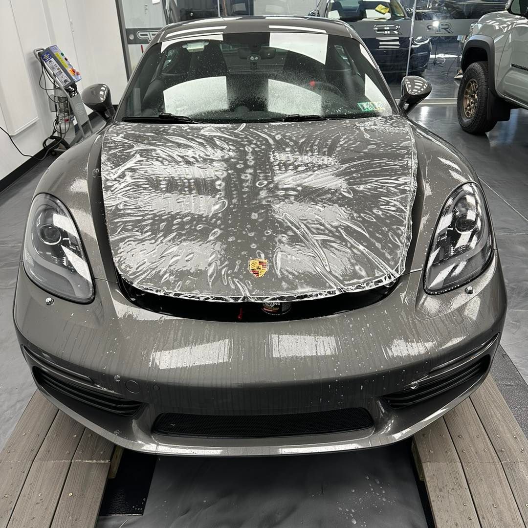 A gray sports car is wrapped in plastic in a garage.