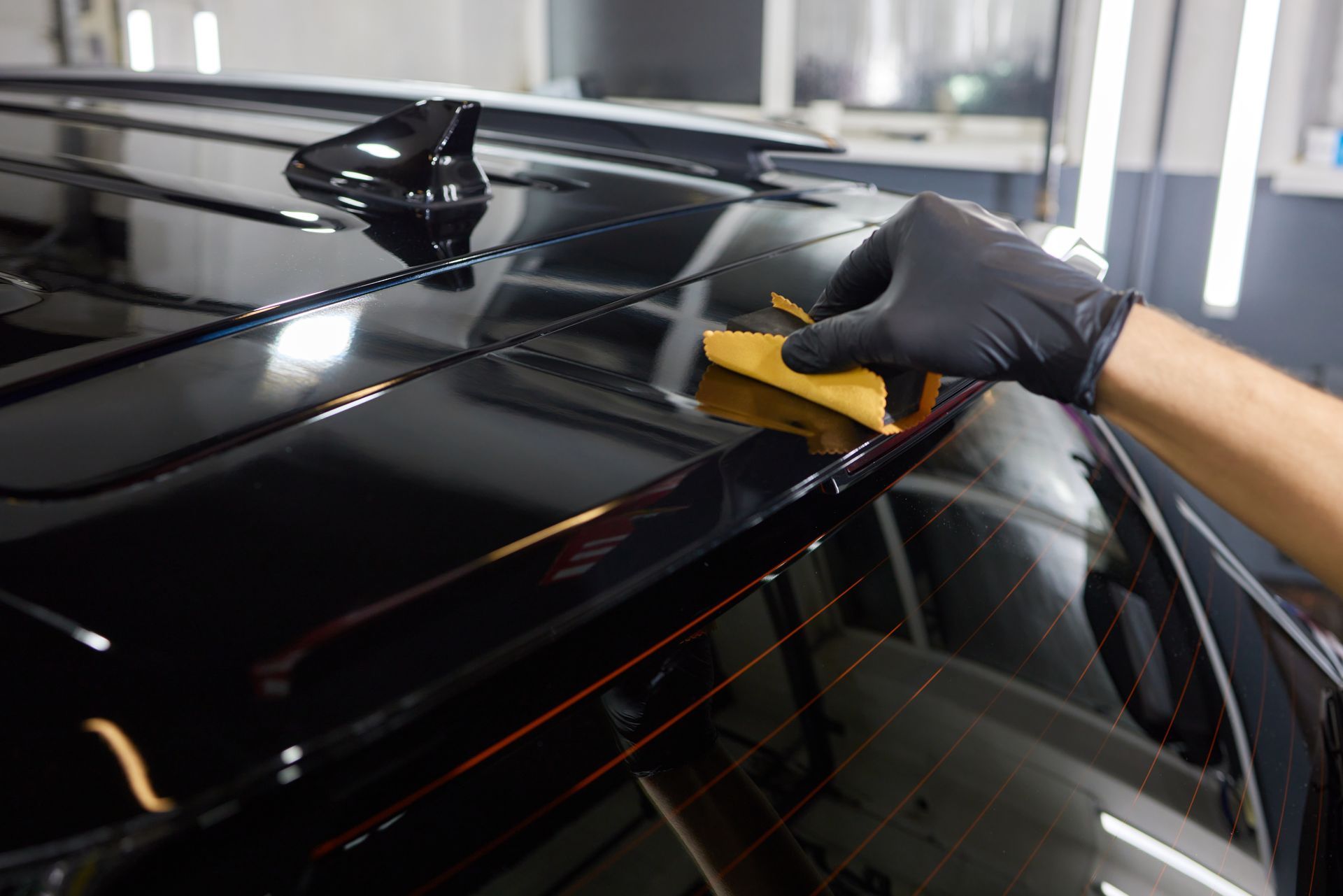 A person is cleaning the roof of a black car with a cloth.