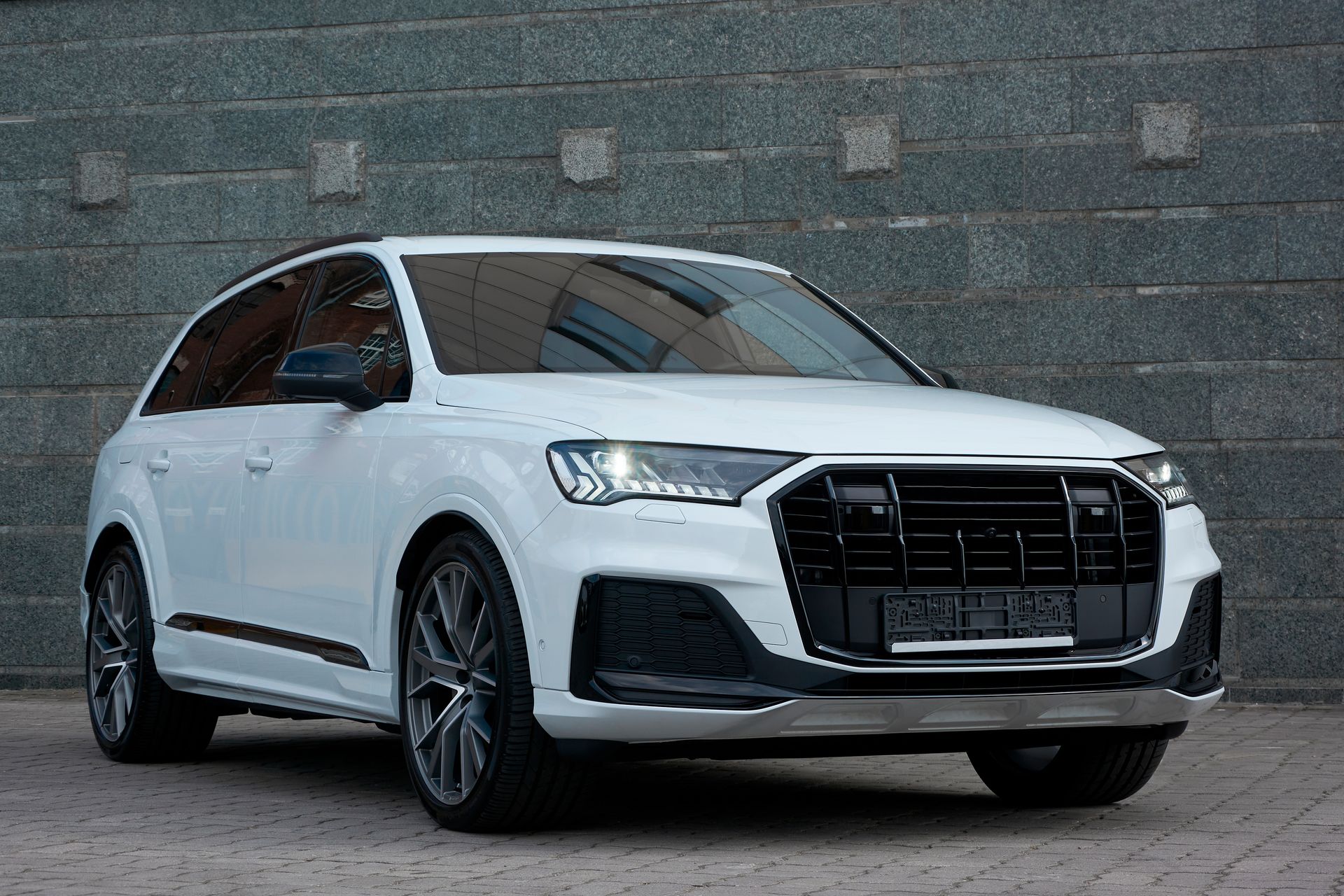 A white audi q7 is parked in front of a brick wall.