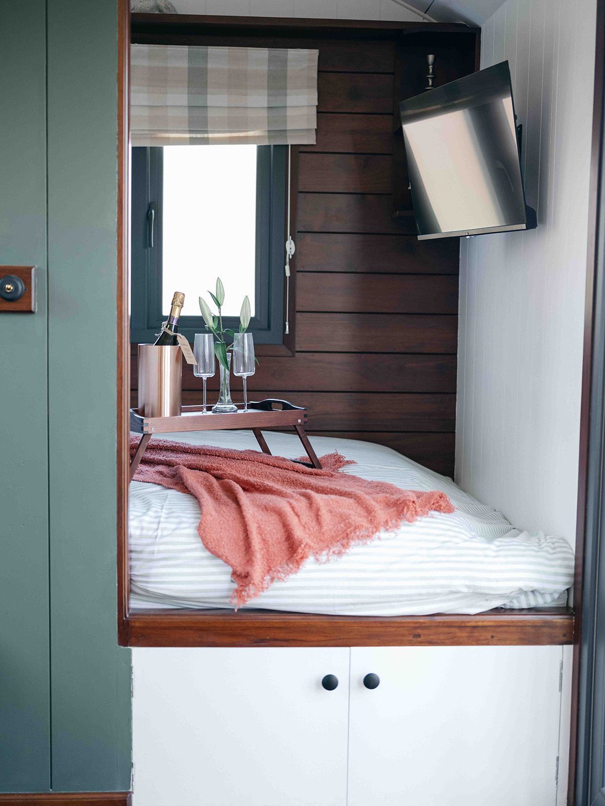 Small bedroom nook with a bed, pink throw, window, and wall-mounted TV.