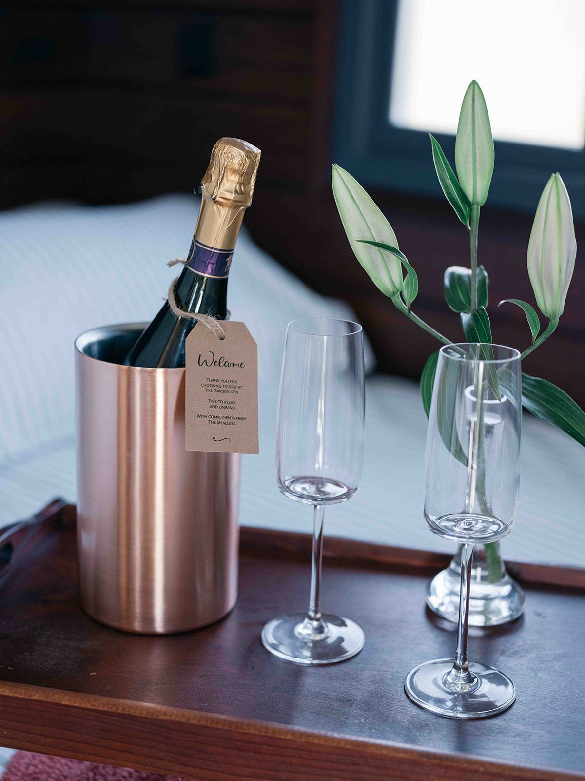 Champagne bottle in a copper ice bucket beside two wine glasses and a small floral arrangement on a table