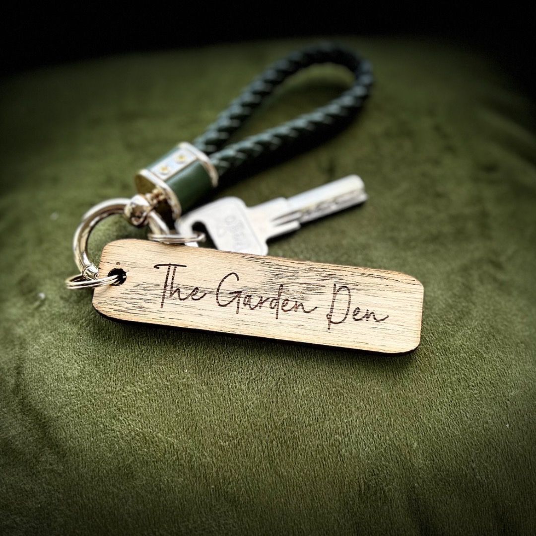 Wooden “The Garden Pen” tag beside a key on a green fabric background