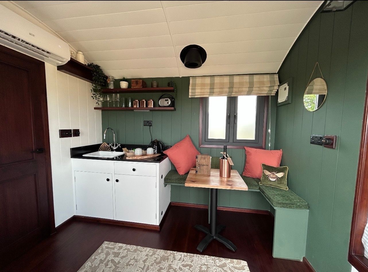 Small cozy room with a white cabinet, bench seating, green walls, and a window with red cushions.