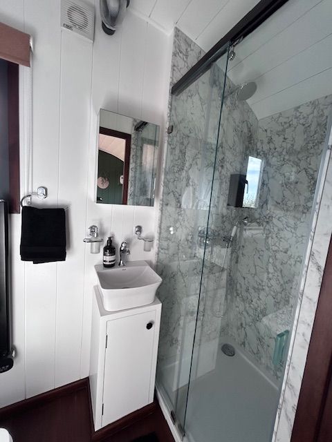 Compact white bathroom with sink, mirror, black towel, and glass shower enclosure with marble-pattern walls