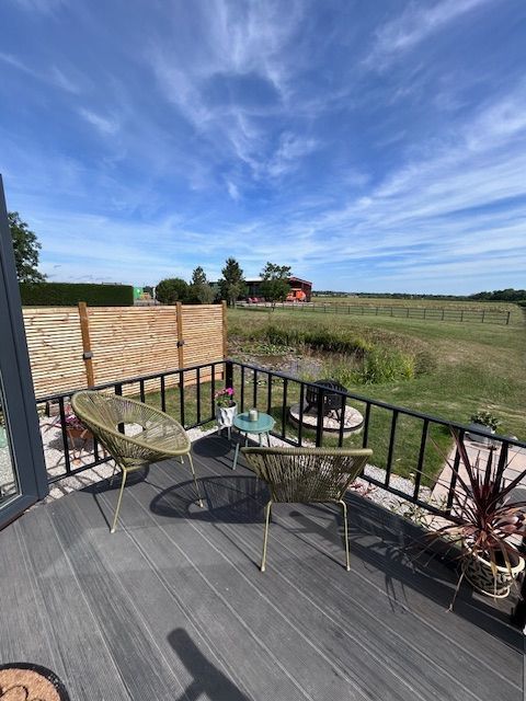 Patio with table and chairs overlooking a grassy field under a blue sky