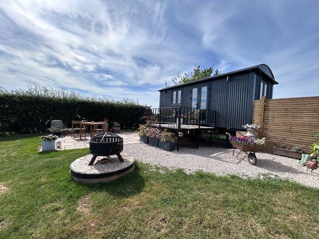 Backyard patio with a black shed, fire pit, outdoor seating, gravel, and grass under a blue sky