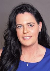 A woman with long black hair is wearing a blue dress and a necklace.