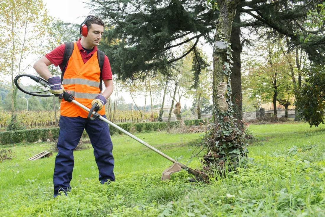 a man wearing headphones is using a lawn mower in a park