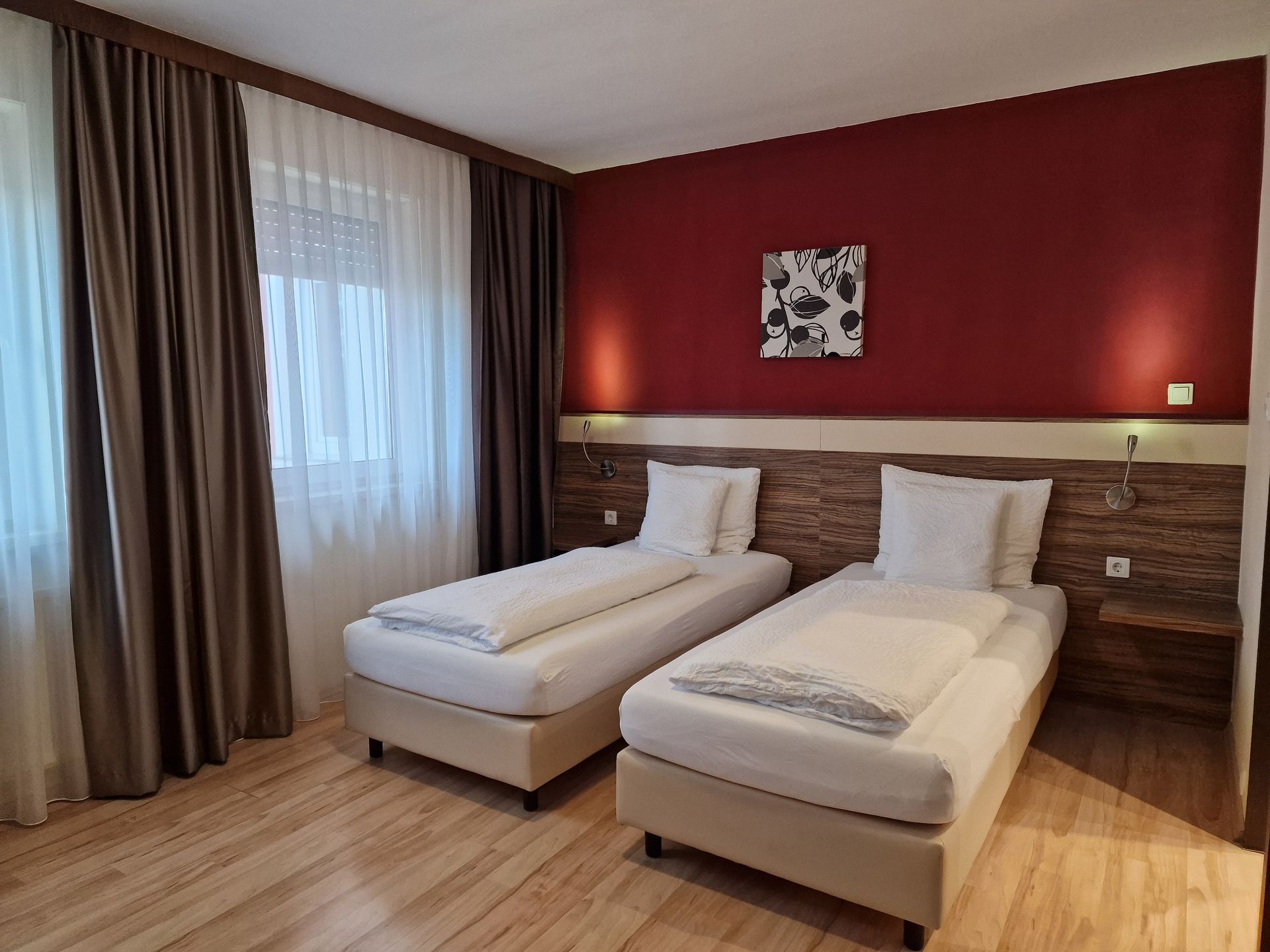 zwei getrennte Betten perfekt für Businessleute. Das Bett steht an einer Weinroten Wand.