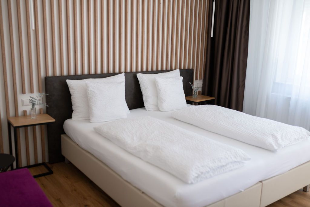 Modernes Schlafzimmer mit Doppelbett, weißer Bettwäsche und Holz-Lamellenwand im minimalistischen Design.