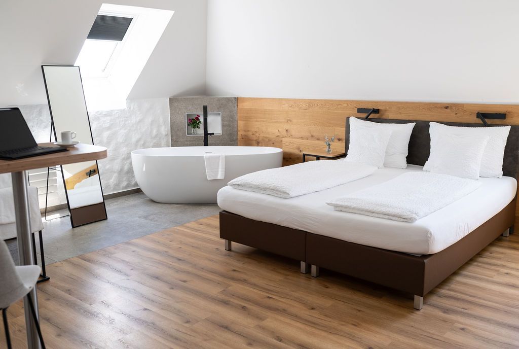 Rooftop Suite mit großem Doppelbett. Freistehende Badewanne neben dem Bett und offenes Badezimmer.