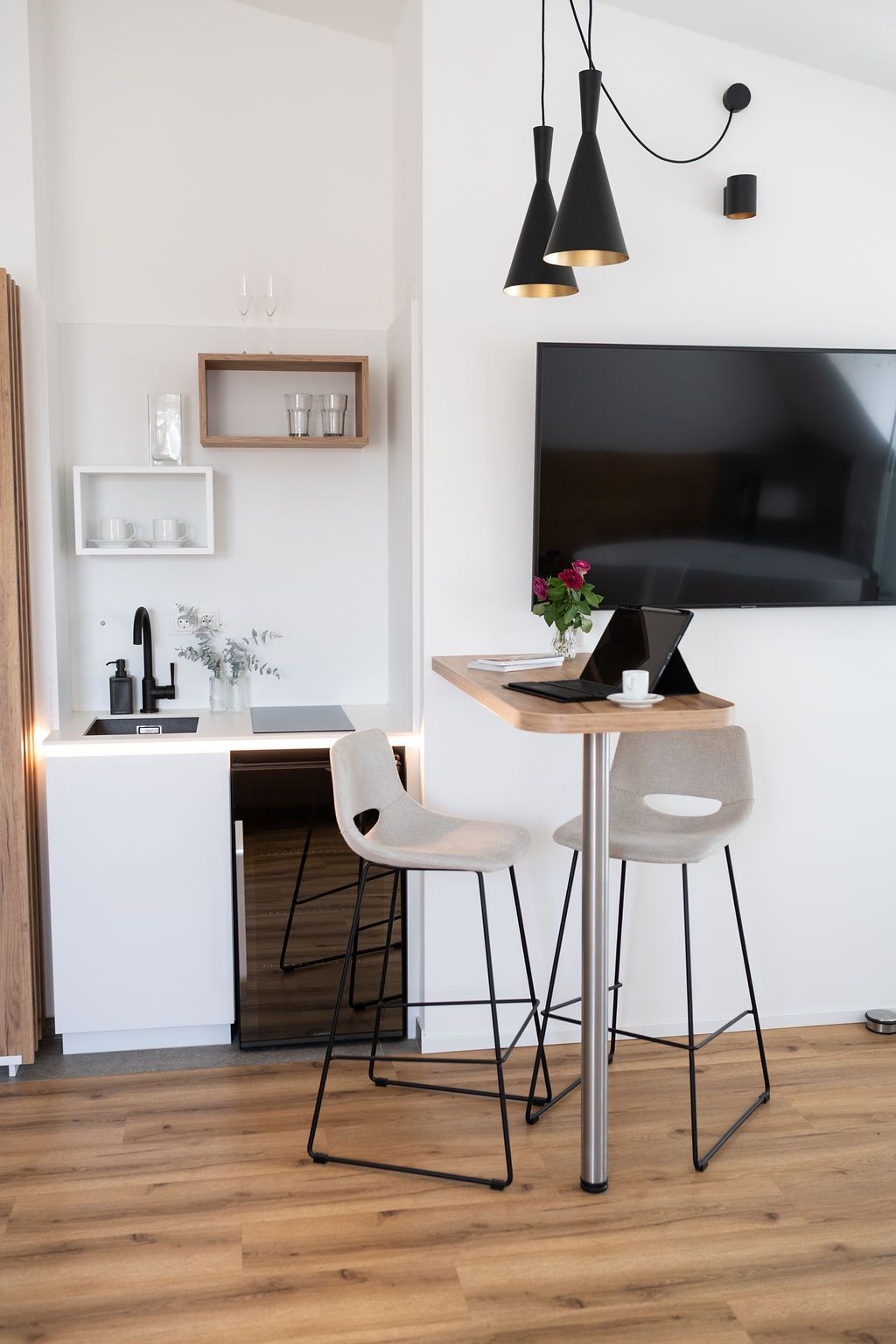 Rooftop Suite mit kleiner Küche und Essbereich. Daneben ein Fernseher und Industrial Style Leuchten über dem Esstisch. 