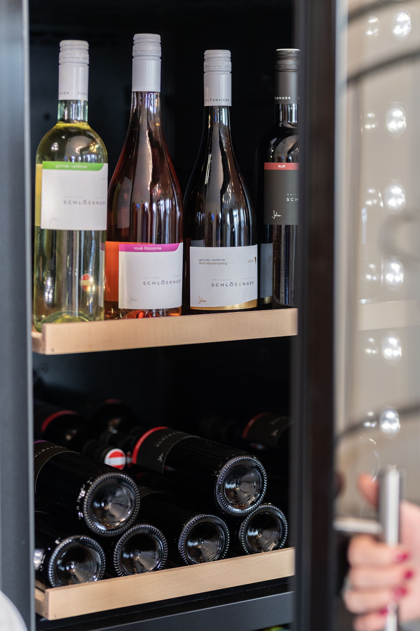 Empfang HotelMaria. Geöffneter Weinkühlschrank mit lokalen Weinen. Der Fokus liegt auf vier unterschiedlichen Weinsorten.