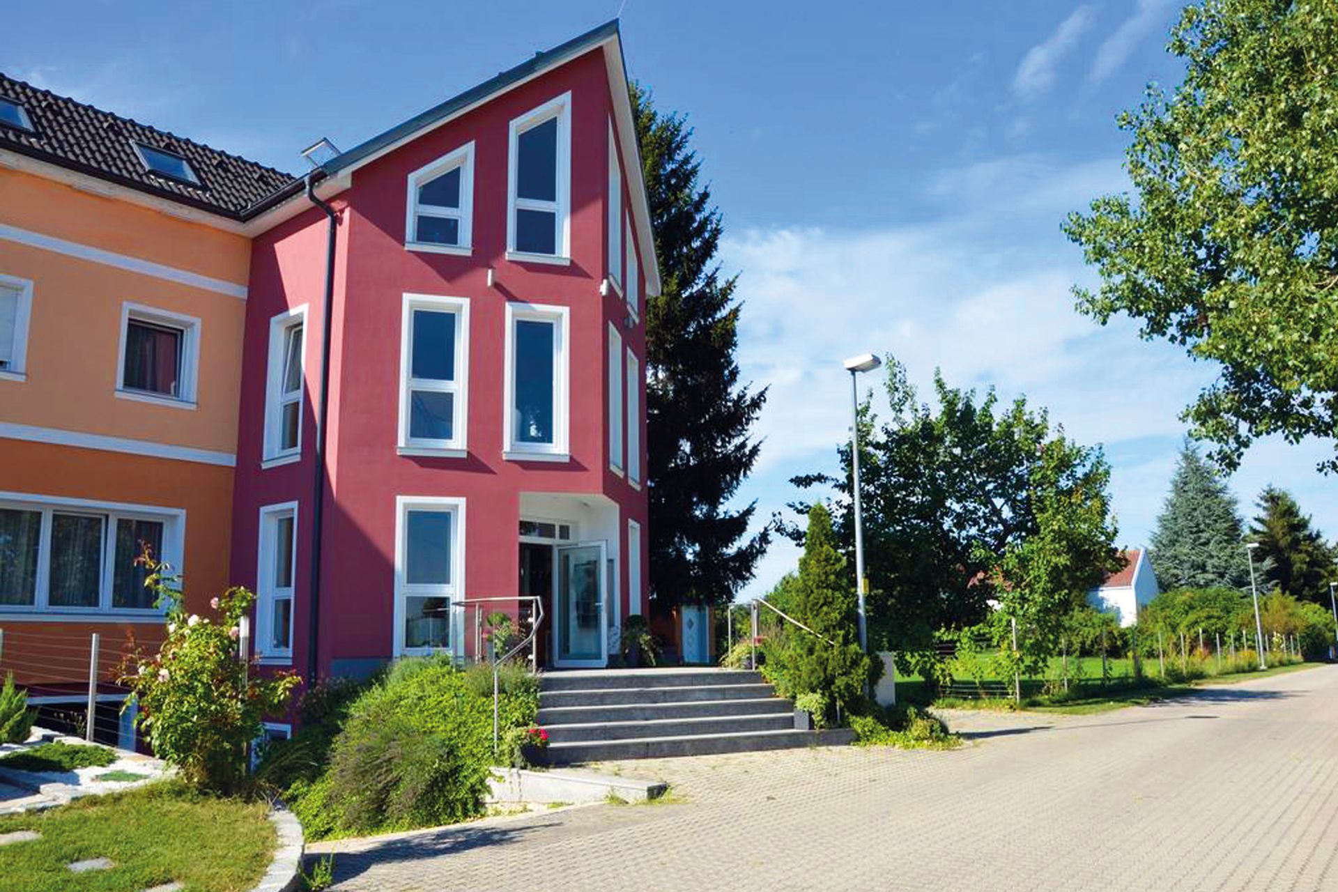 HotelMaria Außenbereich. Rot und orangene Fassade. Stufen führen zur Eingangstüre.