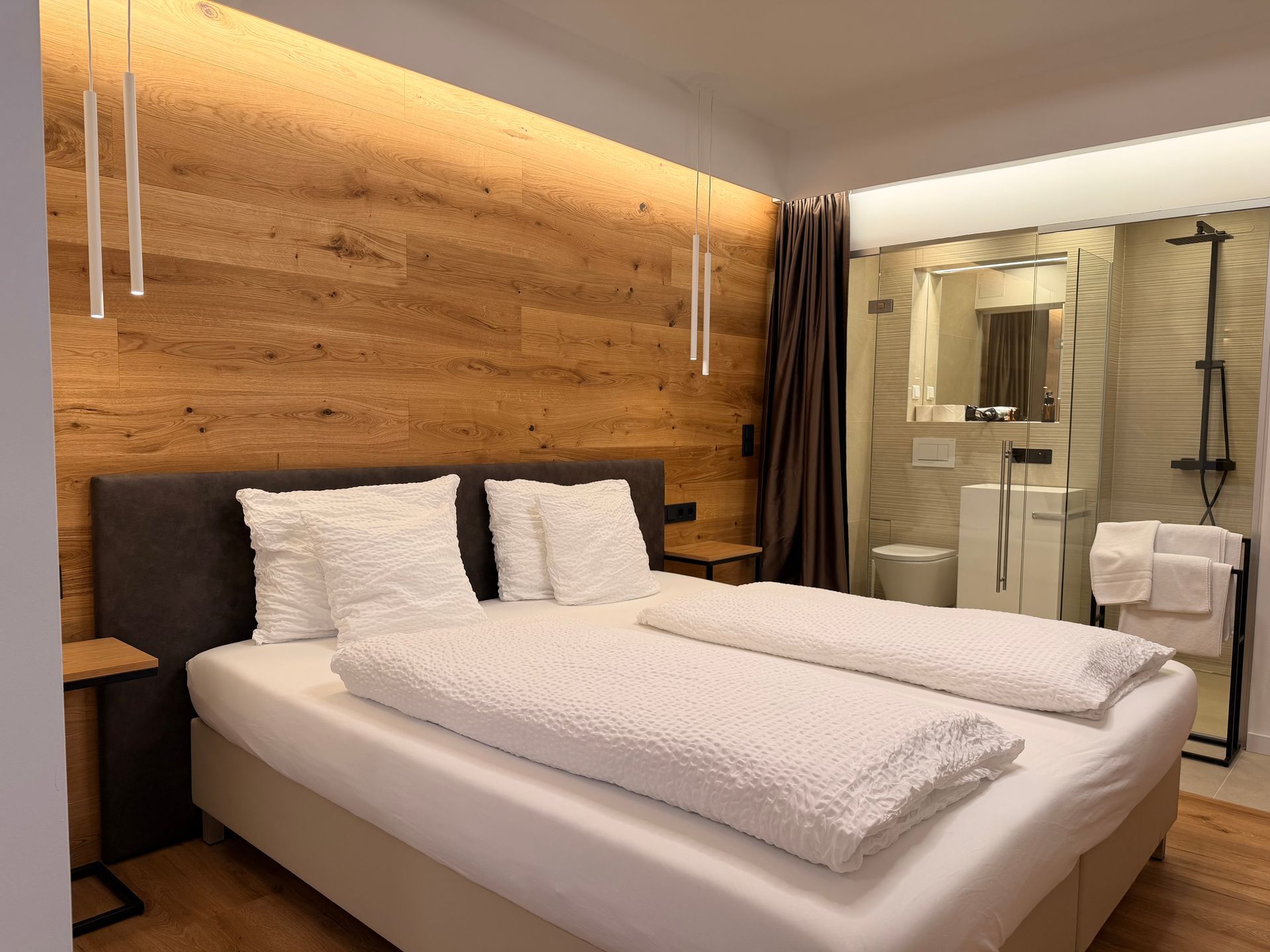 Eiche Queensize. Bett an holzverkleideten Wand. Warme Beleuchtung