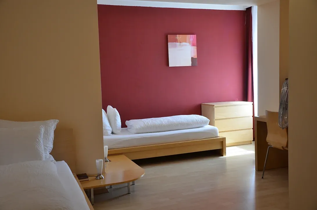 zwei getrennte Betten perfekt für Businessleute. Das Bett steht an einer Weinroten Wand.