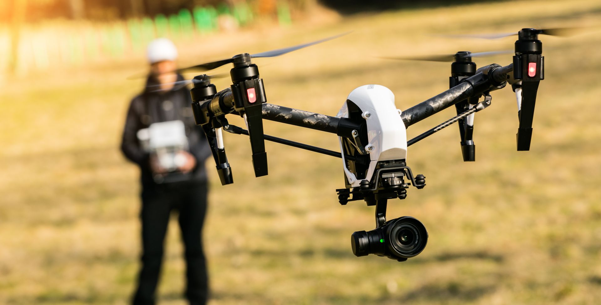 A man is flying a drone in a field with a camera attached to it.