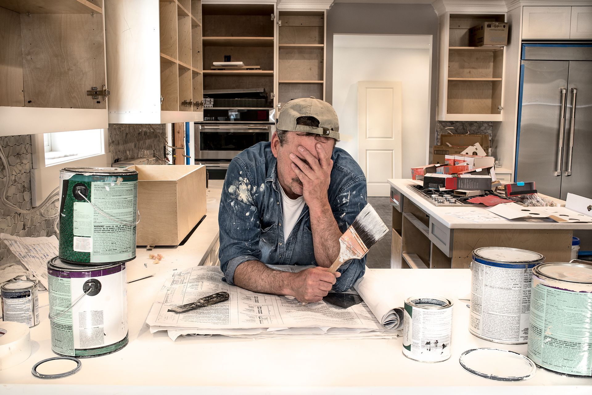 A man is sitting at a table in a kitchen with paint cans.