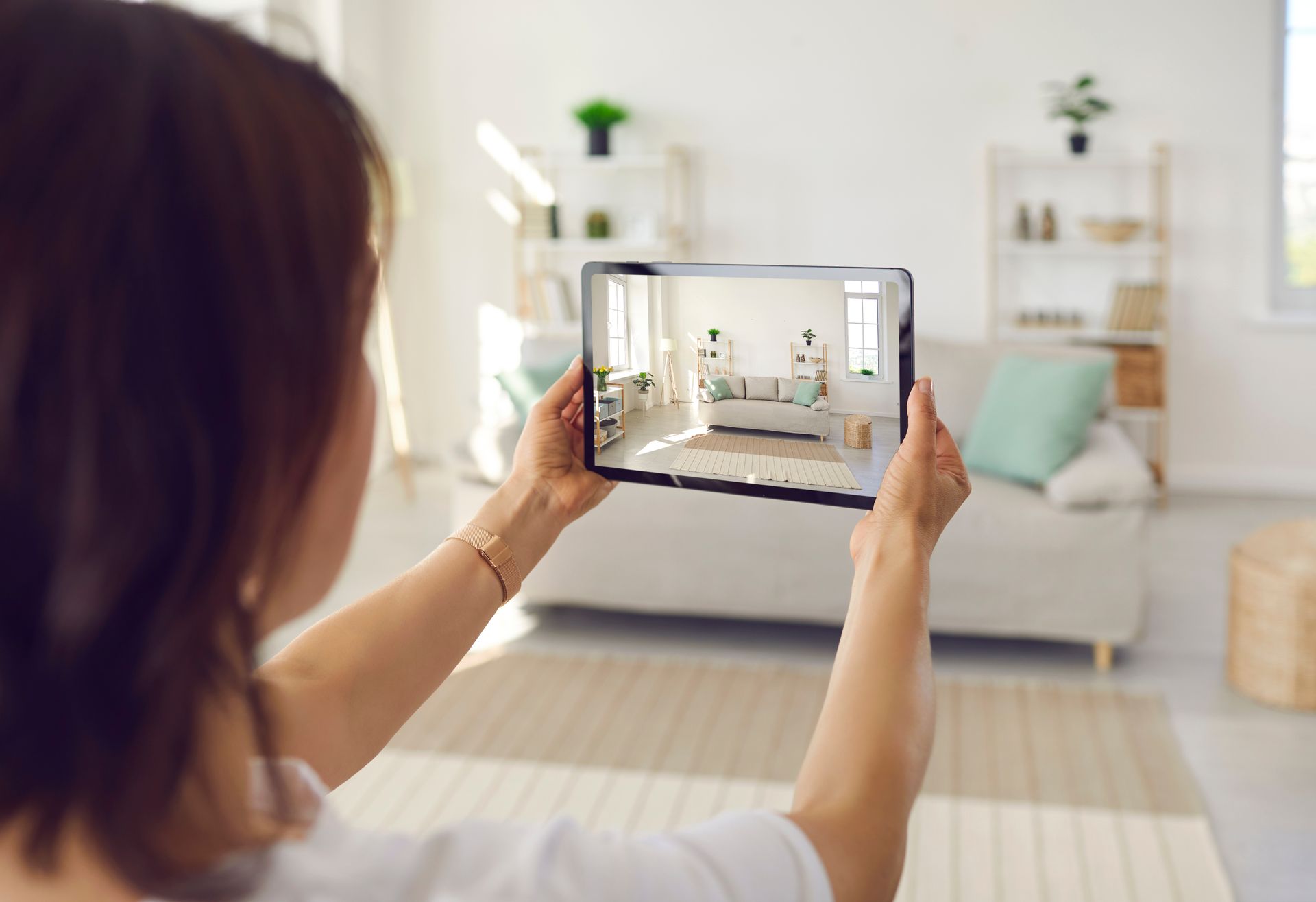 A woman is holding a tablet in her hands and taking a picture of a living room.