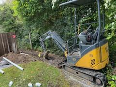 A small excavator is digging a hole in a backyard.