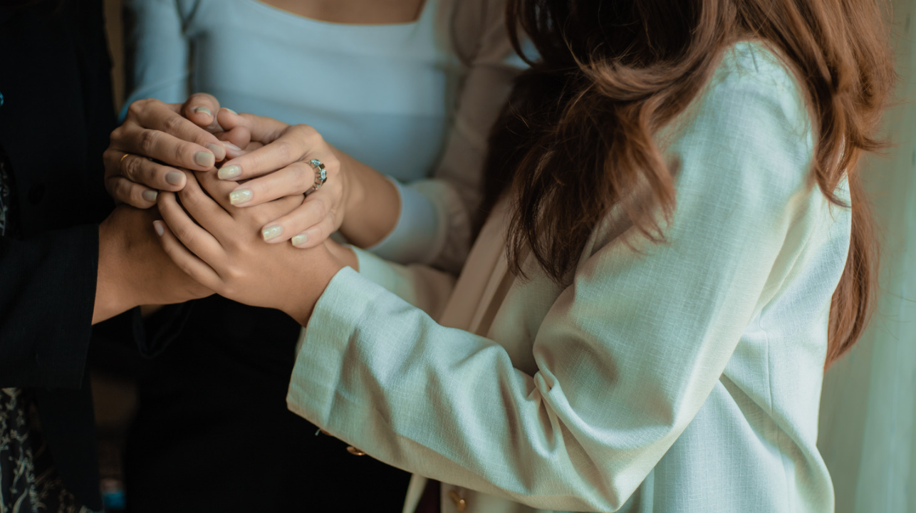 Two people holding hands, one in a light blue top and the other in a pale green shirt.