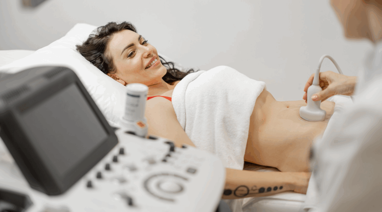 Woman receiving an ultrasound exam on a hospital bed, with monitor and probe visible.