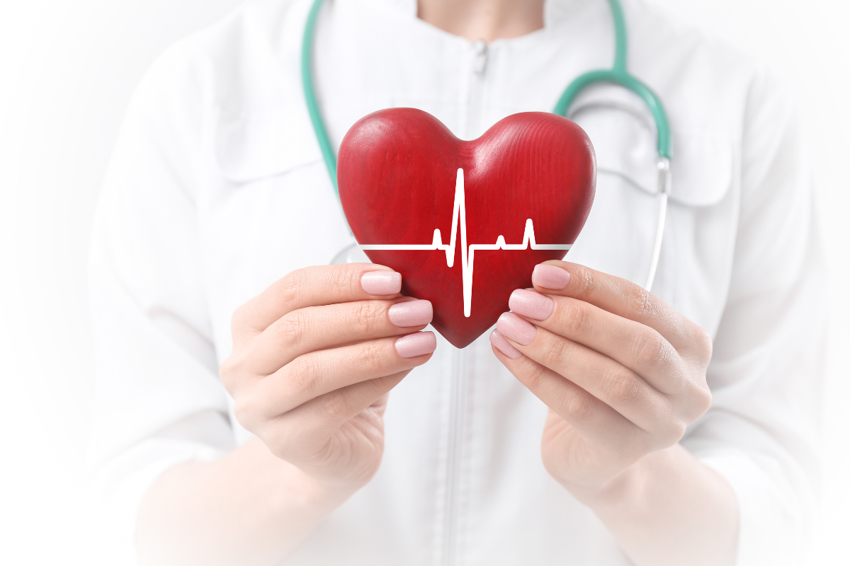 Médico segurando um coração vermelho com uma linha de ECG, tendo como fundo um jaleco branco.