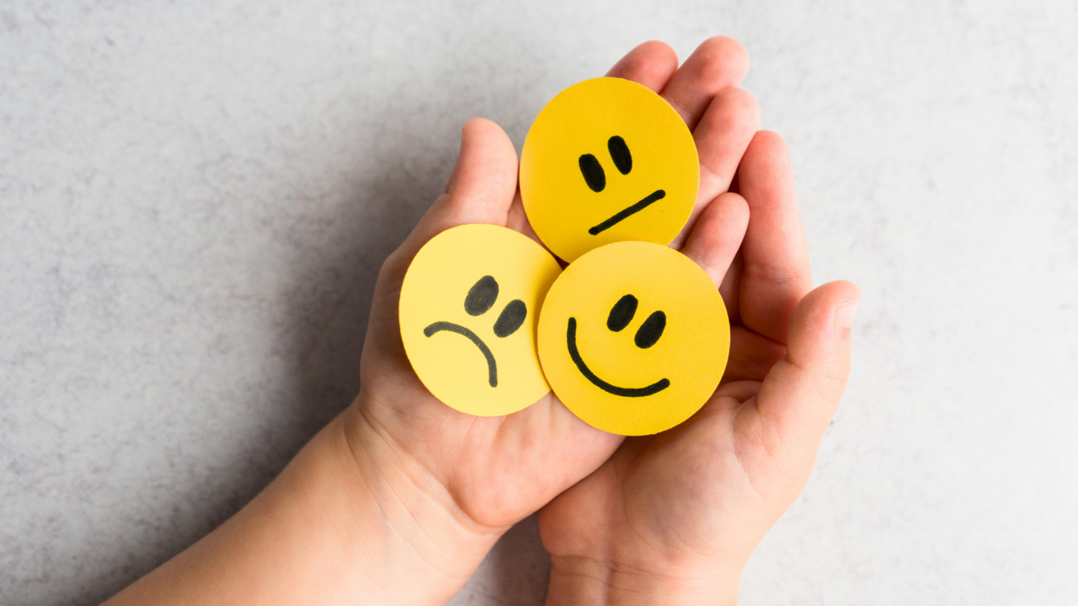 Hand holding three yellow smiley face tokens, one happy, one neutral, one sad.