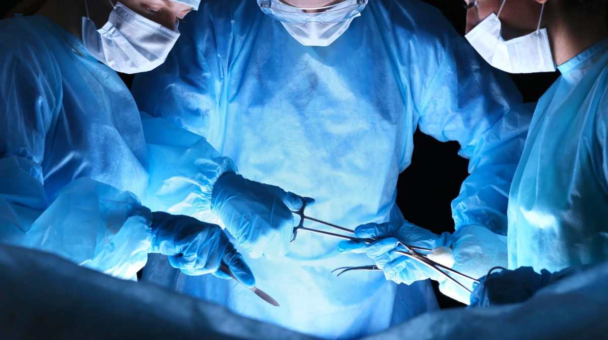 Surgeons in blue scrubs and masks performing an operation under bright operating room lights