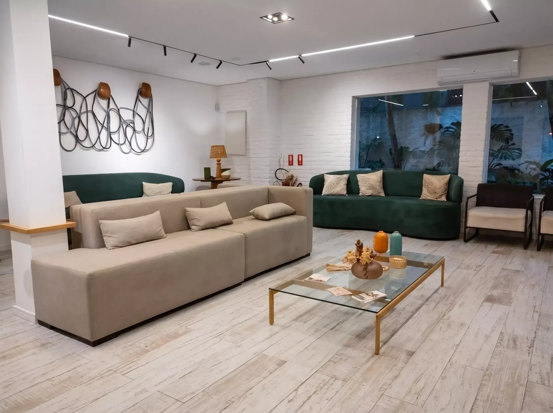Sala de estar moderna com sofás bege e verde, mesa de centro de vidro e janelas amplas.