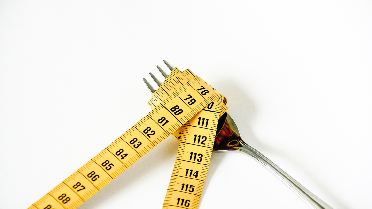 Yellow measuring tape wrapped around a fork and spoon on a white background