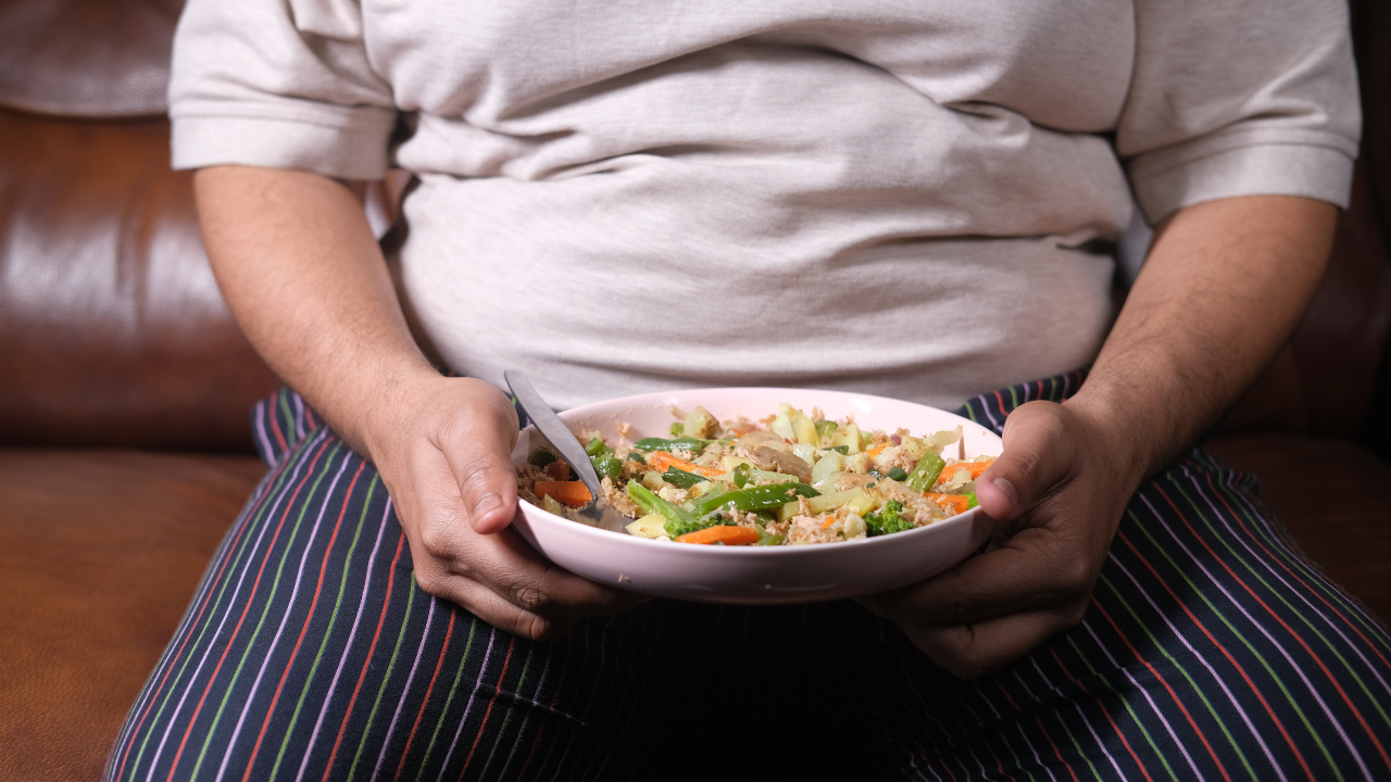 Person holding a bowl of salad while sitting on a couch in striped pants