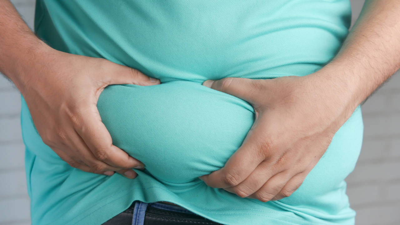 Hands holding a large roll of belly fat against a turquoise shirt.