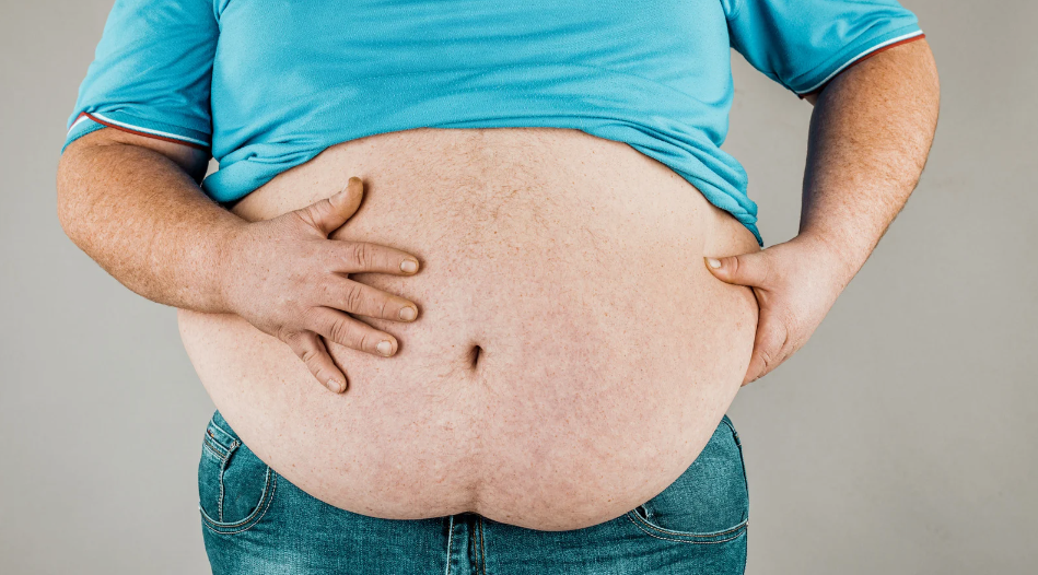 Person in a blue shirt and jeans holding their stomach with hands on their belly.
