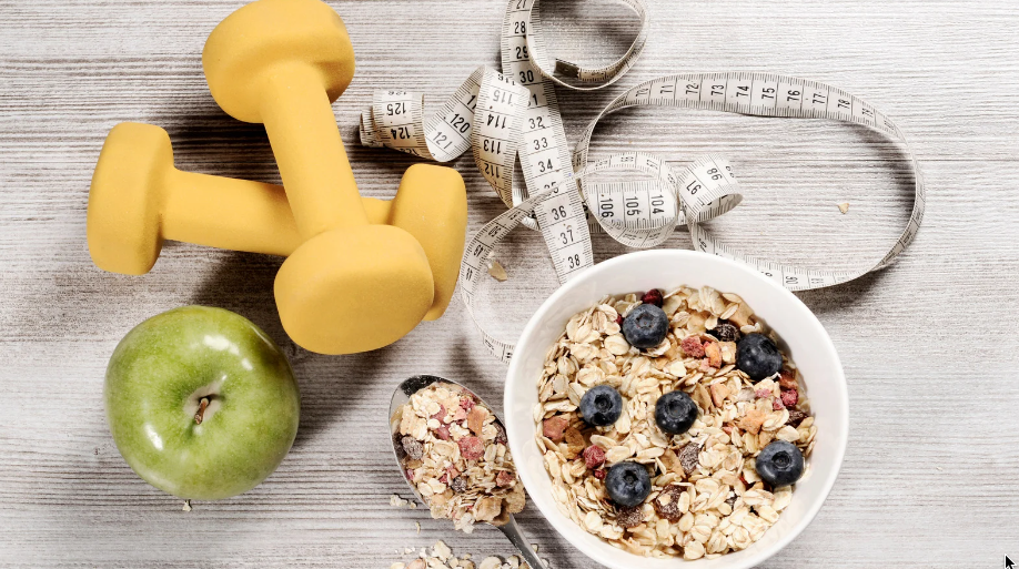 Dumbbells, measuring tape, apple, and oatmeal with berries on a light wood table