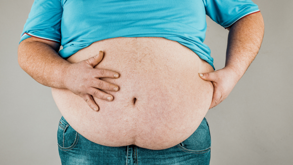 Pessoa de camisa azul e calça jeans segurando a barriga, exibindo o abdômen descoberto.
