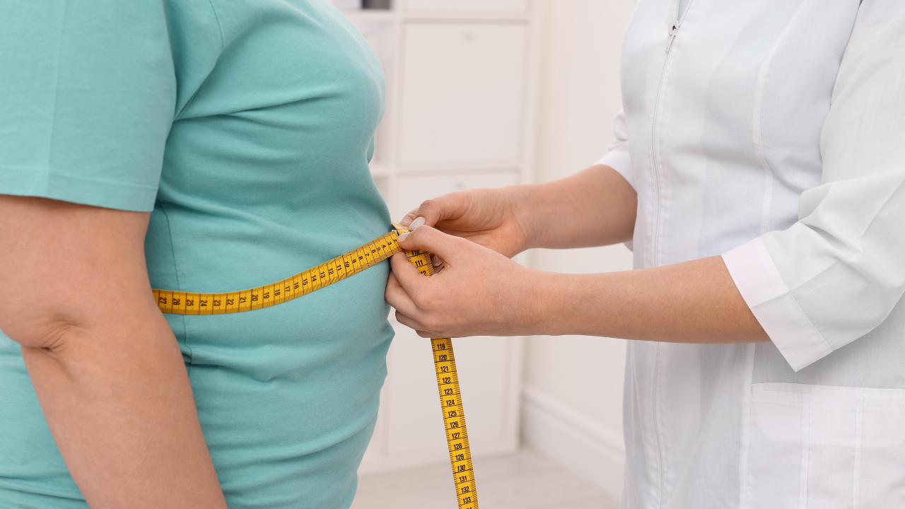 Tailor measuring a person’s waist with a yellow tape measure in a bright room