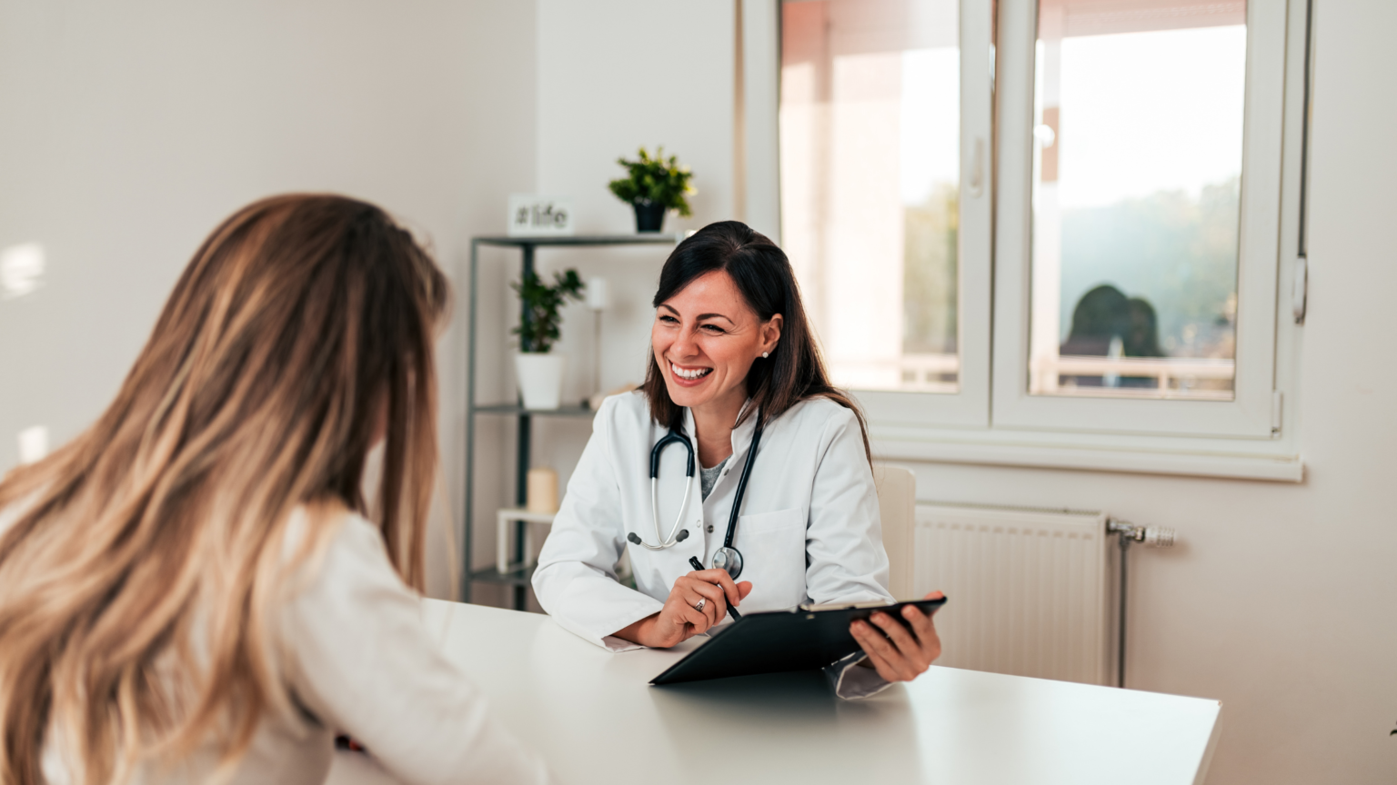 Doctor speaking with a patient across a desk in a bright clinic office