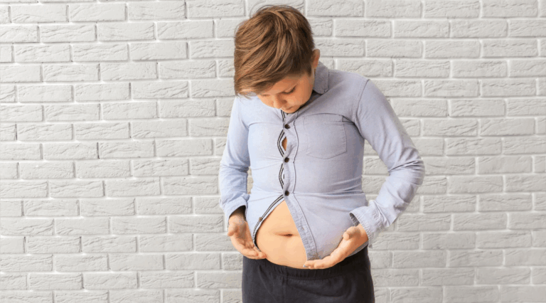 Pessoa levantando uma camiseta cinza para revelar uma barriga, tendo como fundo uma parede de tijolo