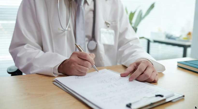 Médico fazendo anotações em uma prancheta, em uma mesa, em um consultório iluminado.