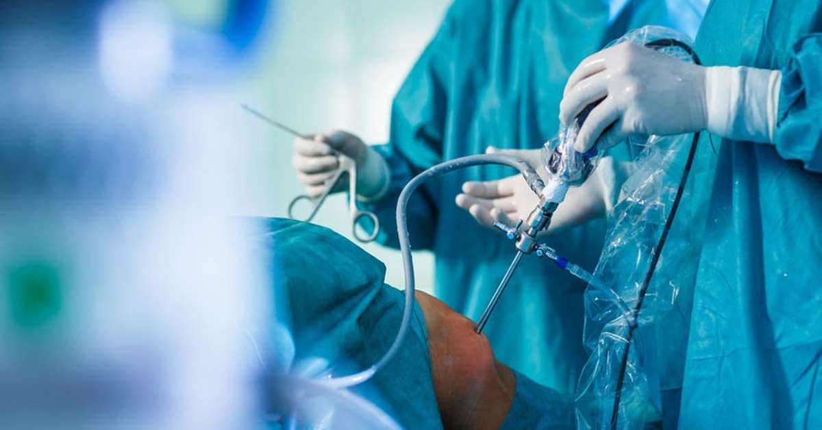 Cirurgiões vestindo roupas cirúrgicas azuis realizam uma operação em uma sala de cirurgia.

