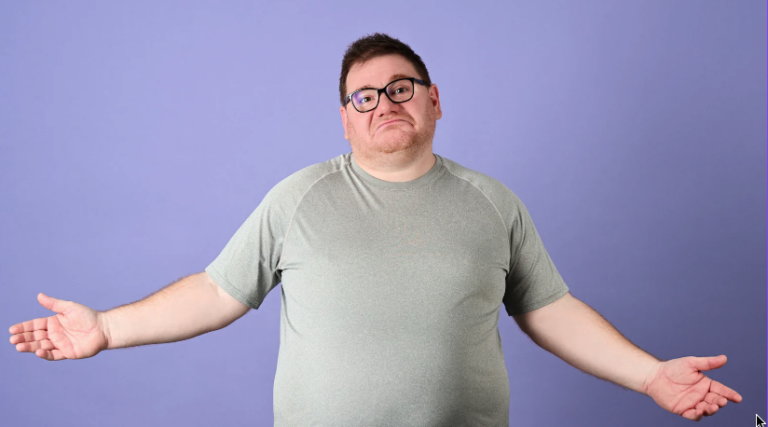 Pessoa de óculos e camisa cinza encolhendo os ombros contra um fundo roxo.
