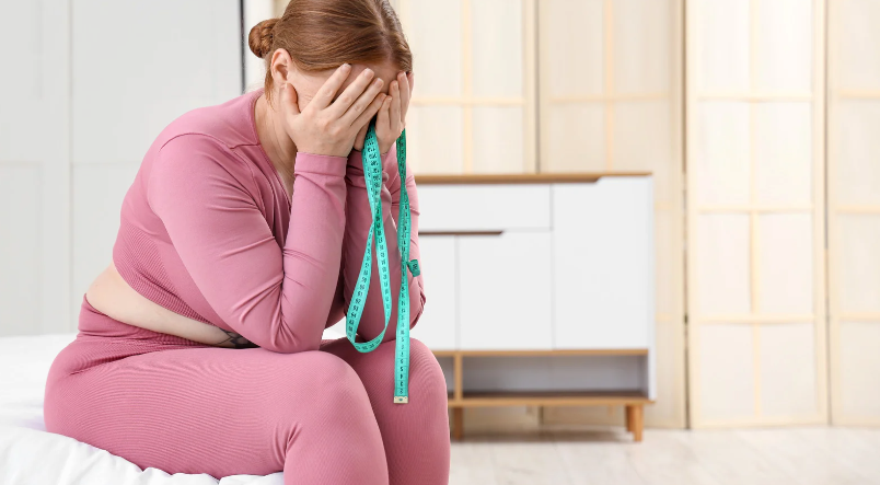 Woman in pink sitting on the floor, covering her face with her hands and holding a jump rope.