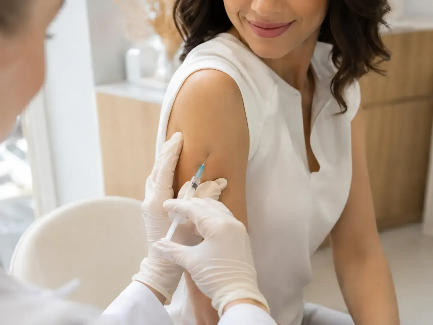 Profissional de saúde aplicando uma injeção em um paciente sorridente em uma clínica bem iluminada.