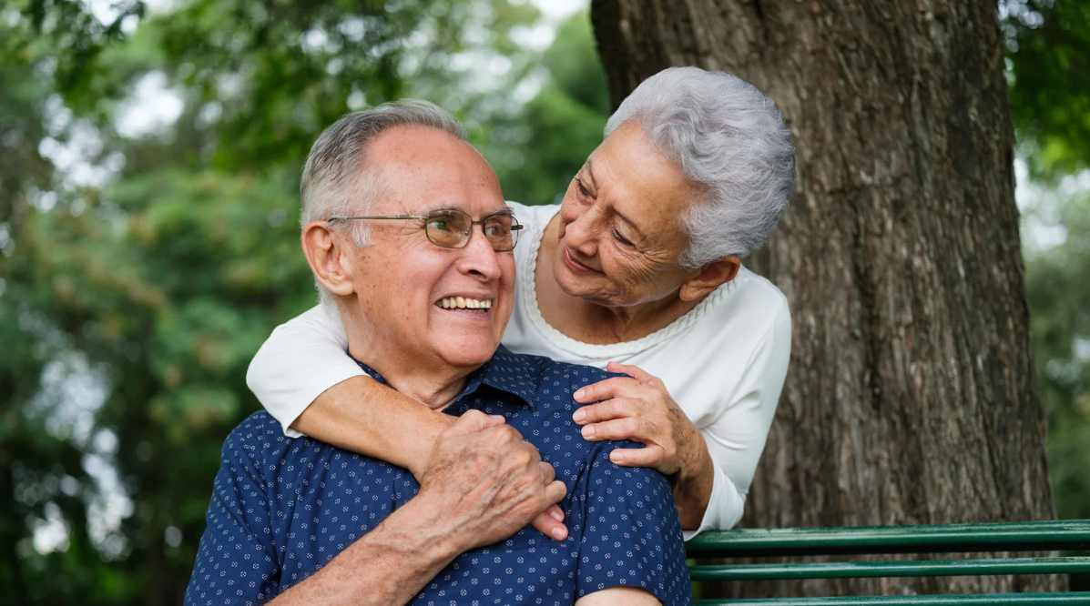 Two adults smiling and hugging on a park bench outdoors