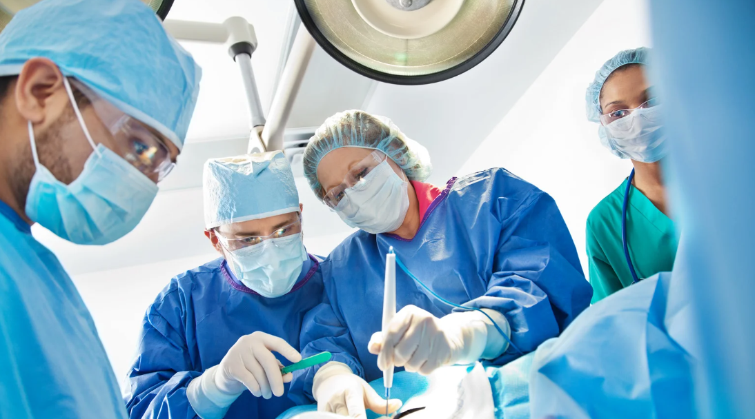Surgeons in blue scrubs and masks performing an operation under bright surgical lights