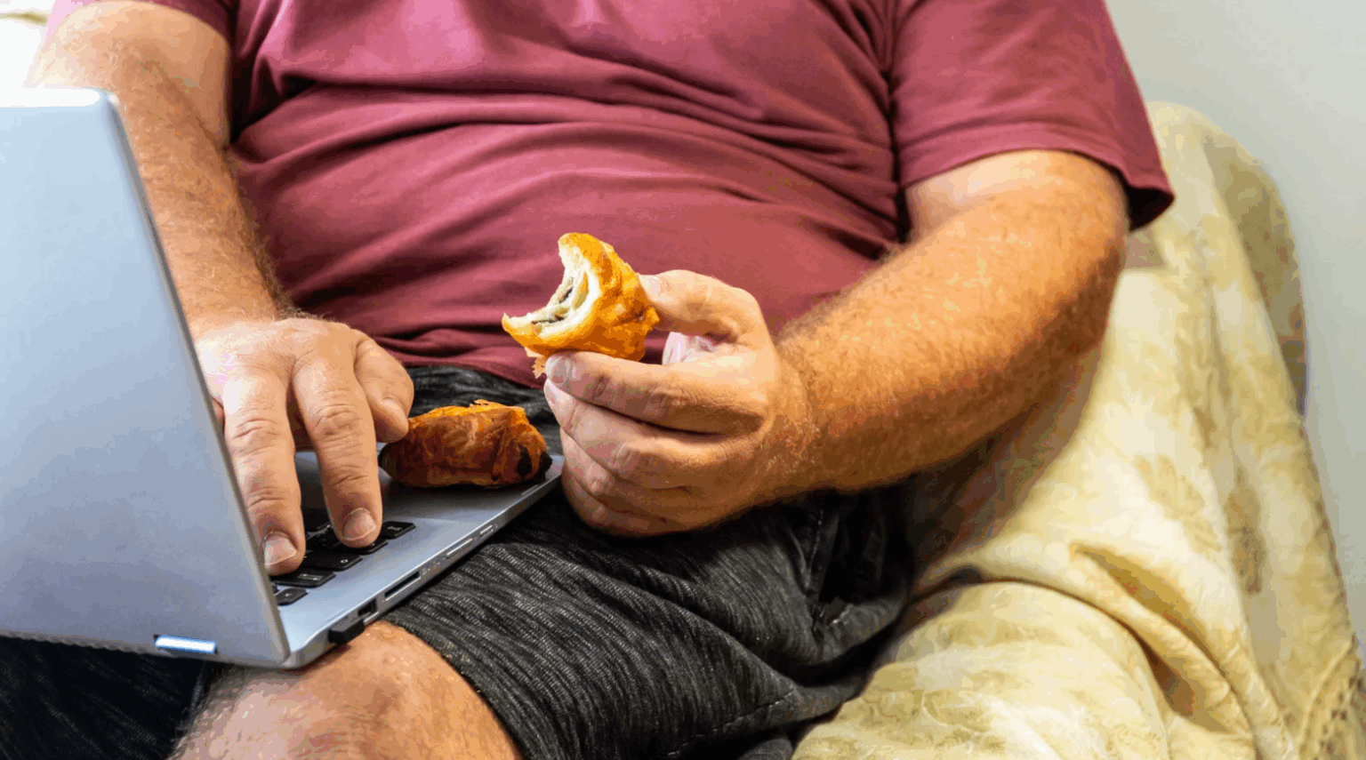 Person on couch using a laptop while holding a slice of pizza