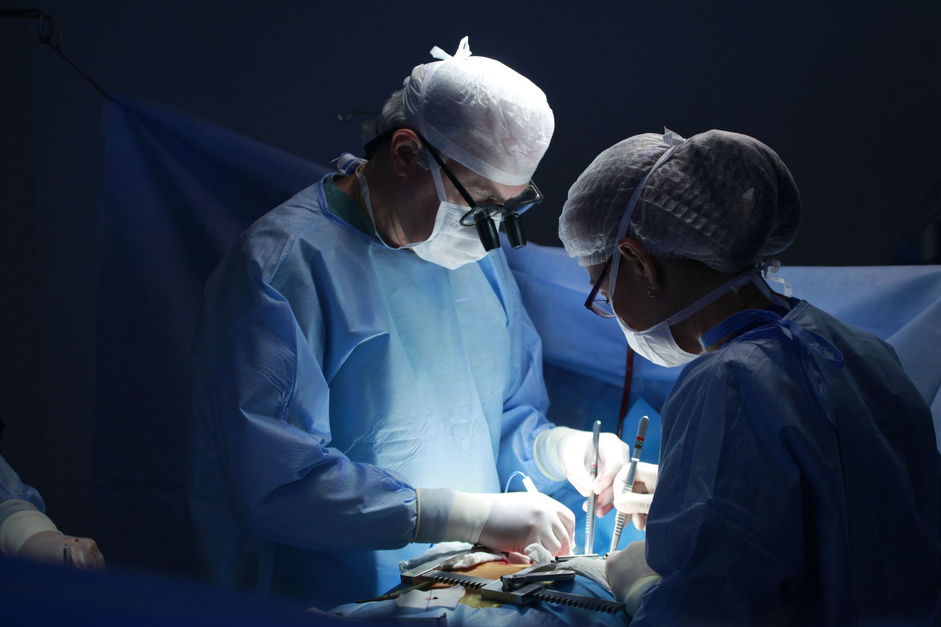 Surgeons in blue scrubs performing an operation under bright operating room lights